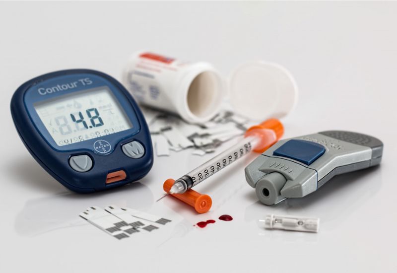 Imagem de monitor de glicose, seringas, medidor de glicemia e remédios, representando a diabetes e doenças cardíacas.