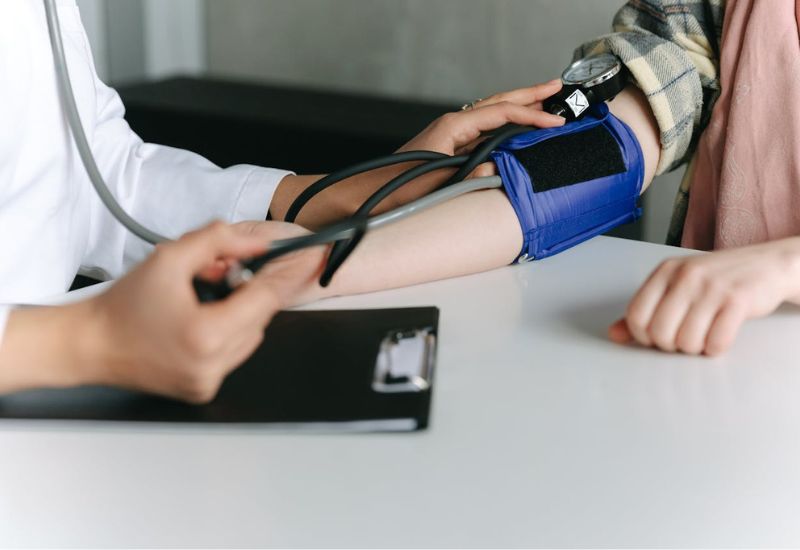 Um profissional de saúde medindo a pressão arterial de um paciente usando um esfigmomanômetro, representando os principais fatores de risco cardiovascular.